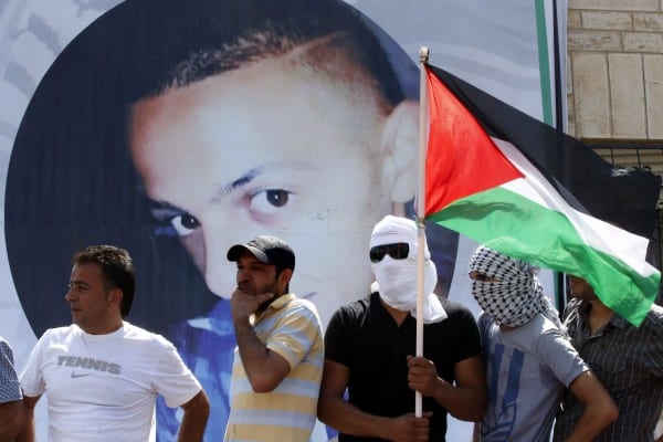 A mourner holds the national flag as mourners gather for the funeral of Palestinian youth Mohammed Abu Khder, 16, (background image) in Shuafat, in Israeli annexed East Jerusalem, on July 4, 2014. Abu Khder, a Palestinian teenager was reportedly kidnapped and killed, triggering violent clashes in east Jerusalem, in an apparent act of revenge for the murder by militants of three Israeli youths.  AFP PHOTO / THOMAS COEX        (Photo credit should read THOMAS COEX/AFP/Getty Images)