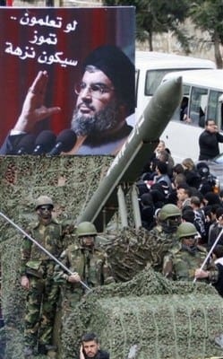Lebanese Hezbollah fighters stand next to a mock rocket under a poster of Hezbollah's leader Sheik Hassan Nasrallah with arabic words reading:" To let you know, July (2006 war) was a picnic," during a demonstration to protest Israel's attack on the Gaza Strip, in the southern market town of Nabatiyeh, Lebanon, on Saturday Jan. 10, 2009. Nearly 20,000 demonstrators marched through the streets of the market town of Nabatiyeh in a rally organized by Hezbollah.
